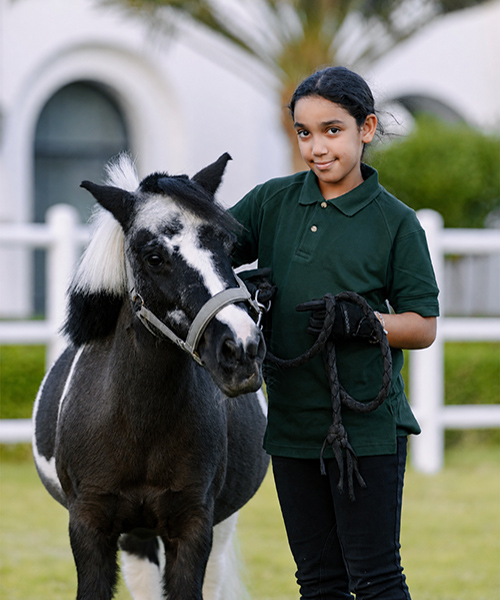 Young rider in ADEC Pony Club uniform standing with a black and white pony at Abu Dhabi Equestrian Club