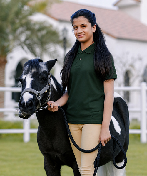 Young rider standing with a saddled black and white pony at ADEC Pony Club